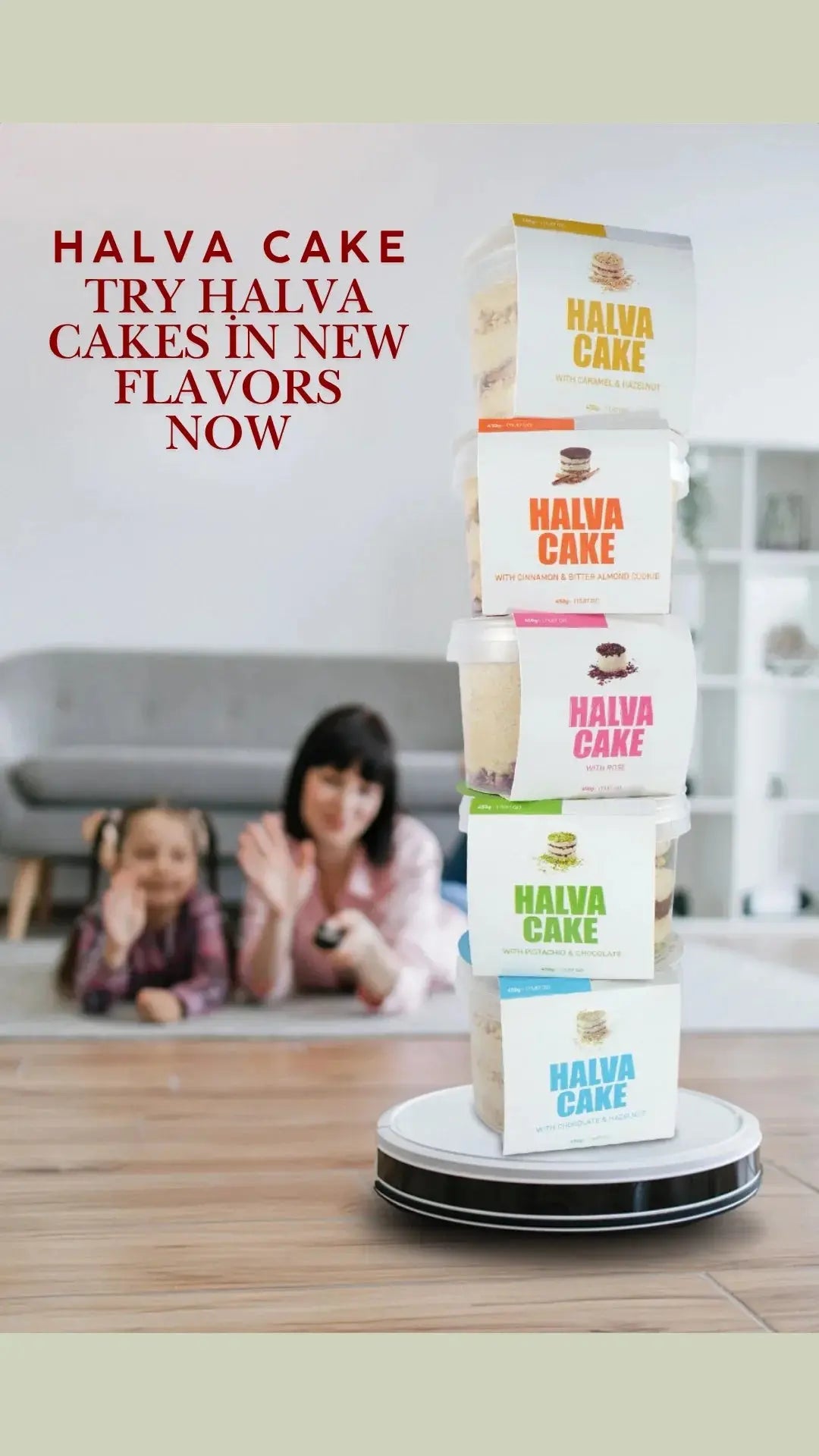 Stacked halva cake containers with new flavors on a robot vacuum, woman and child waving in background.